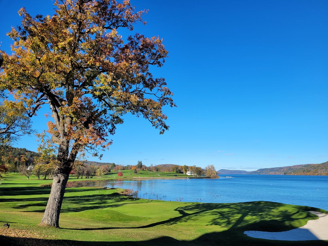 A beautiful golf course by a serene lake with fall foliage and a clear blue sky.